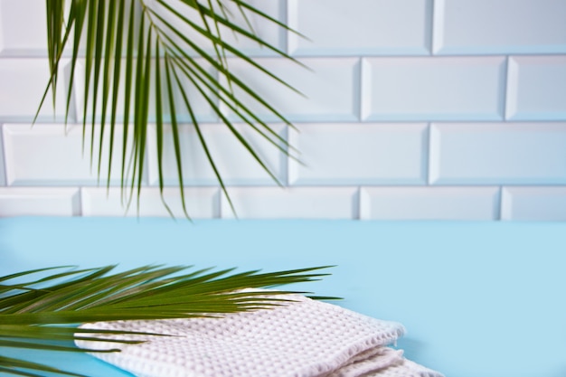 Palm leaf and white waffle towel on the background of tiles in the bathroom. Mockup.