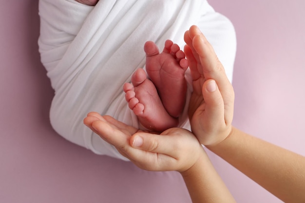 The palms of the father the mother are holding the foot of the newborn baby in a white blanket Feet of the newborn on the palms of the parents Studio macro photo of a childs toes heels and feet