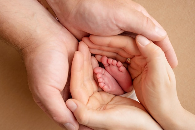 The palms of the parents A father and mother hold the feet of a newborn child The feet of a newborn in the hands of parents Photo of foot heels and toes