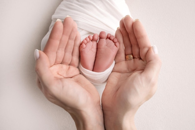 The palms of the parents A father and mother hold the feet of a newborn child in a white blanket on a white background The feet of a newborn in the hands of parents Photo of foot heels and toes