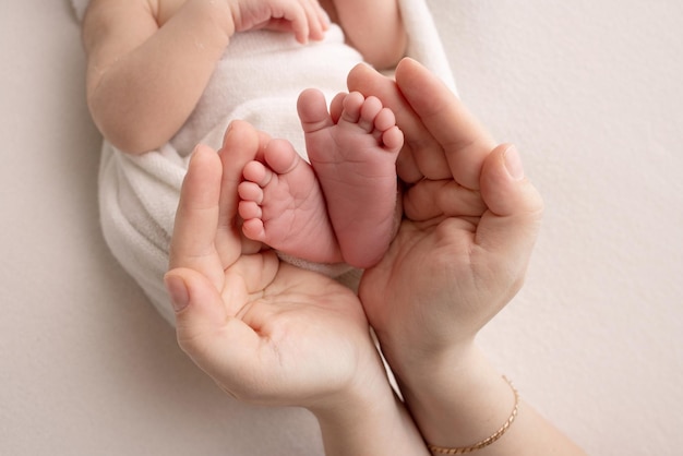 The palms of the parents A father and mother hold the feet of a newborn child in a white blanket on a white background The feet of a newborn in the hands of parents Photo of foot heels and toes