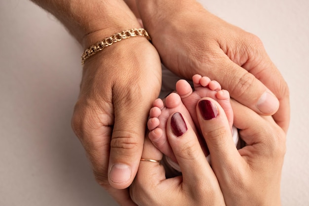 The palms of the parents A father and mother hold the feet of a newborn child on a white studio background The feet of a newborn in the hands of parents Macro Photography of foot heels and toes