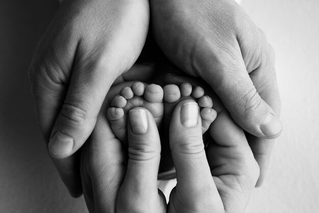 The palms of the parents holds the feet of the newborn child The newborn39s legs are in the hands of the mother39s father Macro photo of foot heels toes