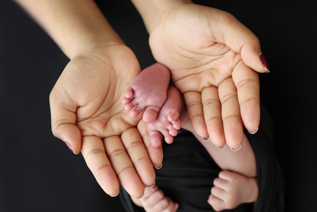 The palms of the parents A mother hold the feet of a newborn child in a black blanket on a Black background The feet of a newborn in the hands of parents Macro Photo of foot heels and toes