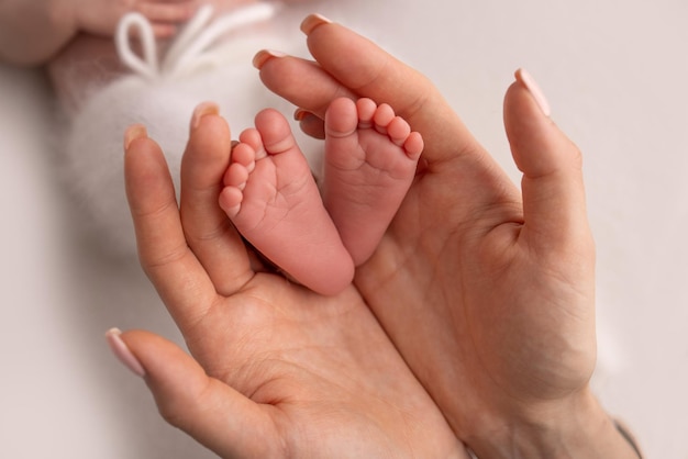 The palms of the parents A mother hold the feet of a newborn child in a white blanket on a white background The feet of a newborn in the hands of parents Photo of foot heels and toes