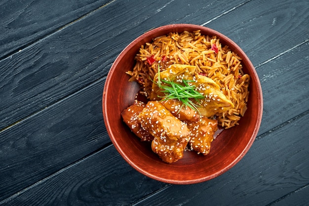 Pan-Asian Street Food - Sweet and Sour Chicken Garnished with Rice, served in a bowl on a wooden surface. Wok rice with chicken. Asian food. Selective focus