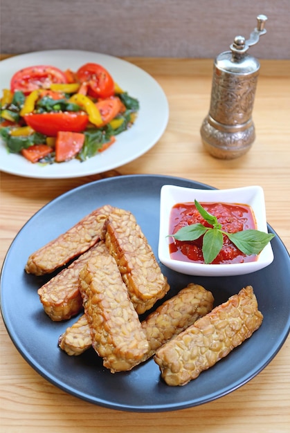 Pan fried Tempeh with homemade marinara sauce with blurry vegetables salad in backdrop