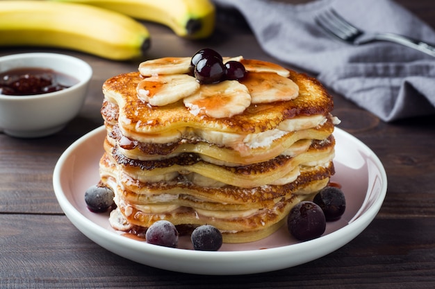 Pancake cake with bananas and berry syrup, selective focus, dark background.