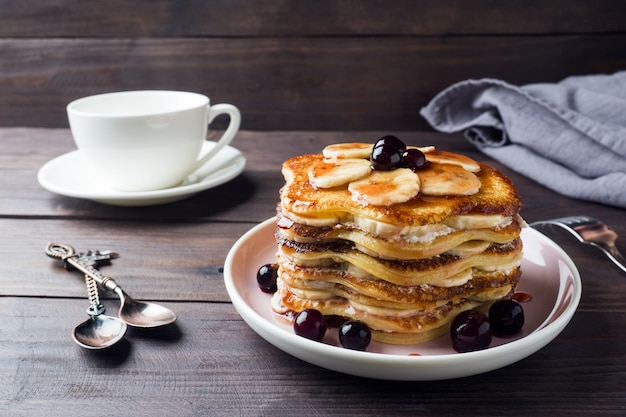 Pancake cake with bananas and berry syrup, selective focus, dark background.