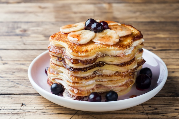 Pancake cake with bananas and berry syrup, selective focus, dark background.