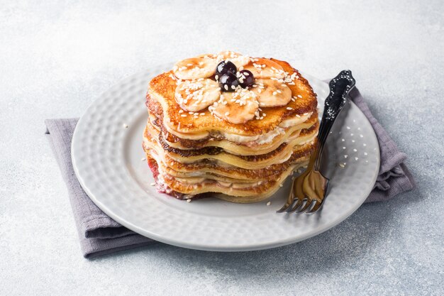 Pancake cake with bananas and berry syrup, selective focus, grey background.