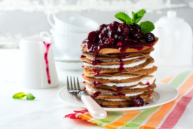 Pancake chocolate cake with cottage cheese filling and cherry sauce on a light background. Selective focus.