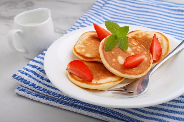 Pancake in a plate with strawberries decorated with mint on a marble table