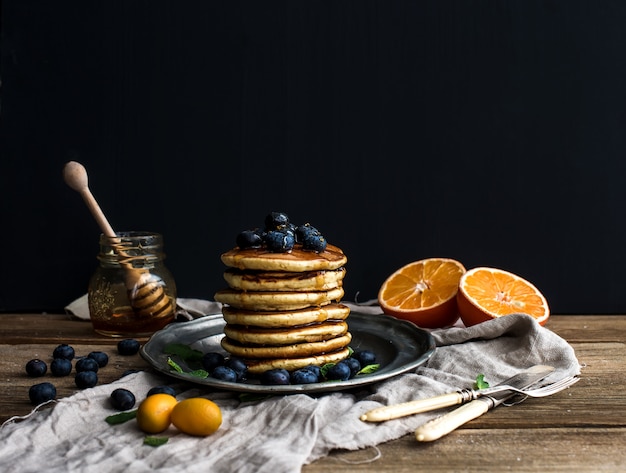 Pancake tower with fresh blueberries, oranges and mint on a rustic metal plate.