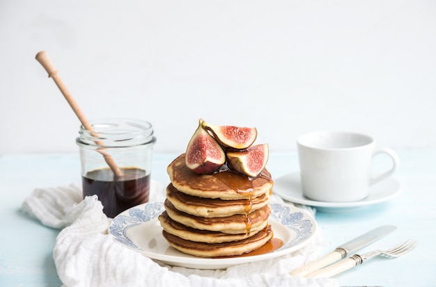 Pancake tower with fresh figs and honey on a rustic plate. White surface