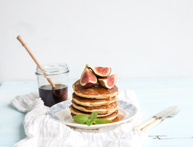 Pancake tower with fresh figs and honey on a rustic plate. White table