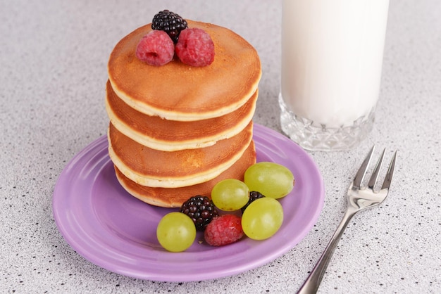 Pancake with berries and glass of milk on table close up