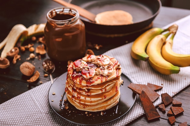 Pancake with chocolate and nut paste, walnuts and banana on a black plate