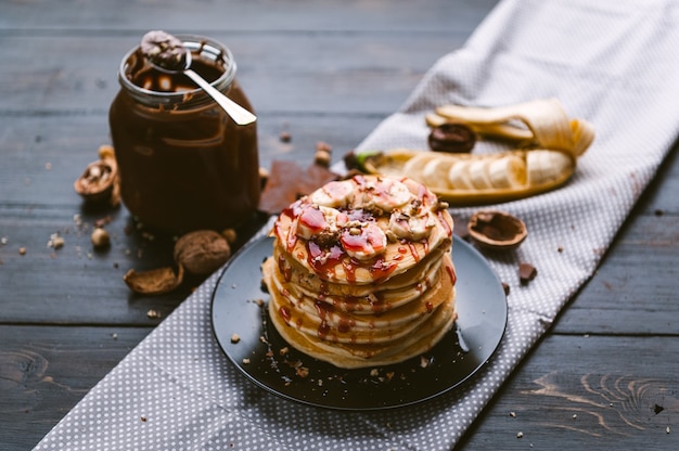 Pancake with chocolate and nut paste, walnuts and banana on a black plate