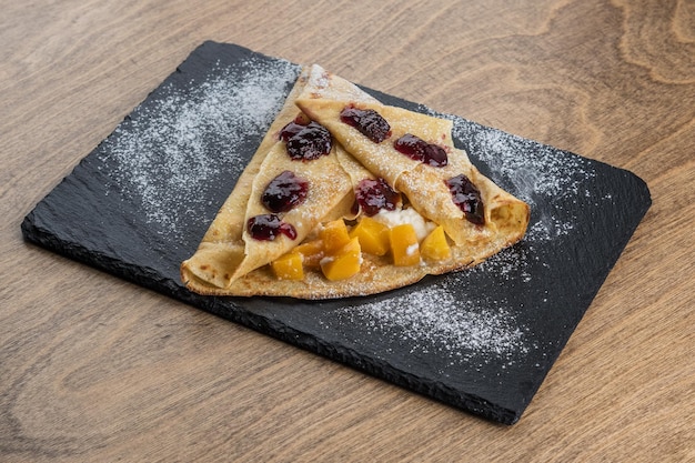 Pancake with peach and strawberry jam on a black tray