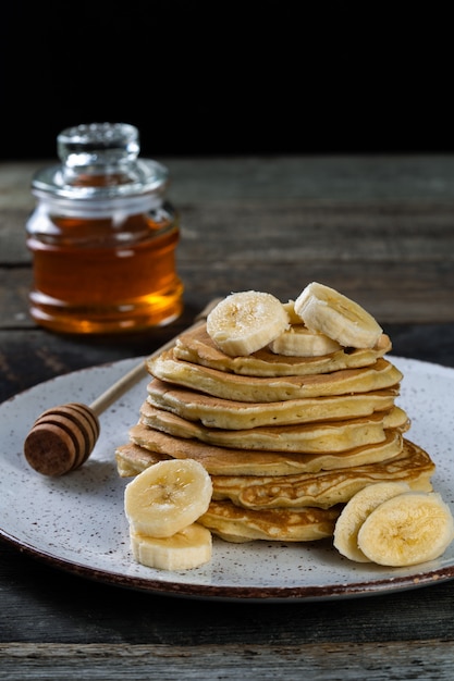 pancakes on the ceramic plate served with bananas and honey on wooden