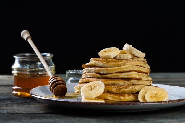 pancakes on the ceramic plate served with bananas and honey on wooden