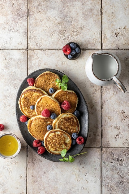 Pancakes in ceramic plate with raspberries blueberries mint leaves honey on a pink tile background top view