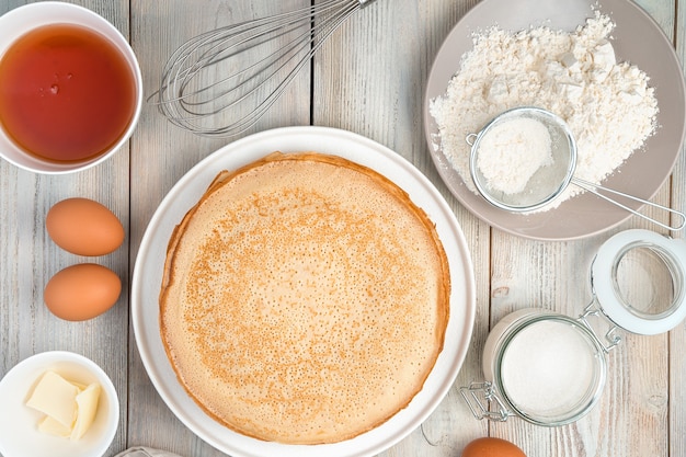 Pancakes and ingredients on a wooden background.