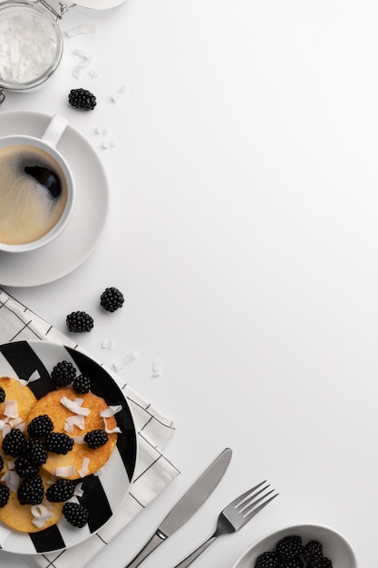 Pancakes made of coconut flour with blackberries and coconut chips on white table