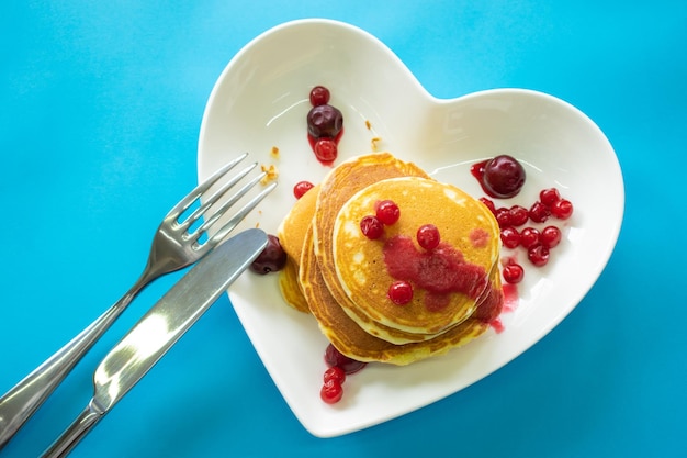 Pancakes on a plate in the form of a heart jam and berries top view