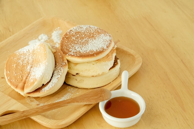 Pancakes, sprinkle icing sugar in a wooden tray. Served with honey in a cup placed on a wooden table.