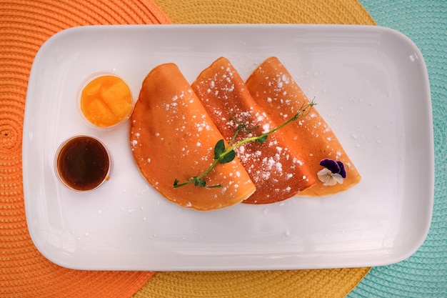 Pancakes on a white plate sprinkled with powdered sugar microgreens and sauces on a plate view from