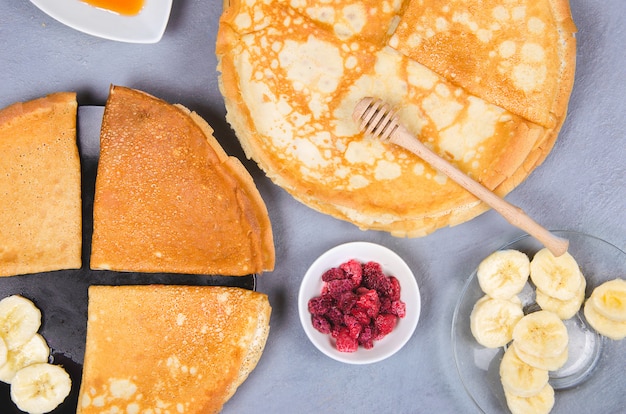 Pancakes with berries and honey for breakfast on gray table