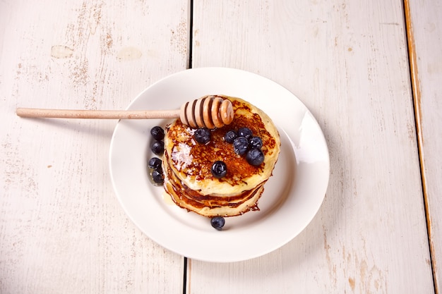 Pancakes with berries and honey on the wooden white table