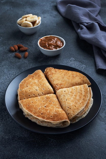 Pancakes with chocolate banana filling Delicious breakfast of pancakes envelopes on a plate dark concrete background