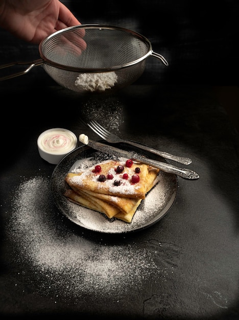 Pancakes with cream and berries and icing sugar on a black tile