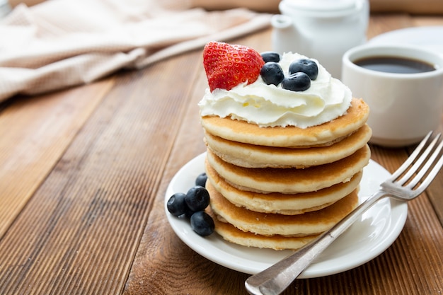 Pancakes with cream, berry and coffee cup over rustic wood