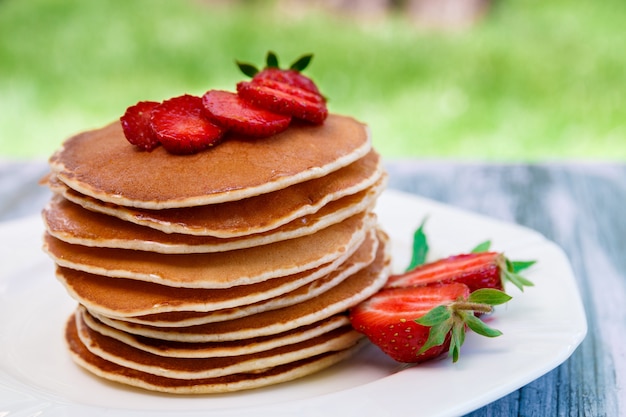 Pancakes with fresh strawberry and mint on white plate on pink wooden   garden or on nature .  Stack of pancakes on table.