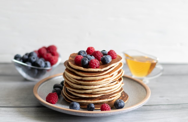 Pancakes with raspberries blueberries and honey on a light background