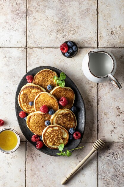 Pancakes with raspberry and blueberry mint leave honey and honey spoon on pink tile background top view