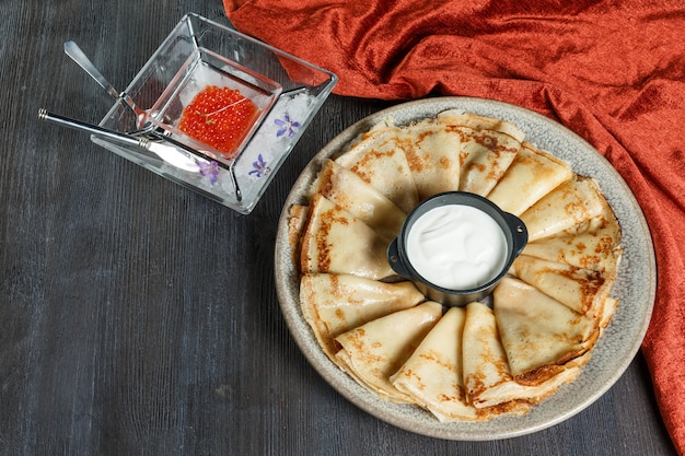 Pancakes with red caviar on a plate. On a wooden background. Top view. Free space for text.