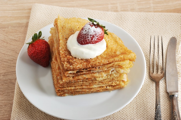 Pancakes with sour cream and strawberries in a plate