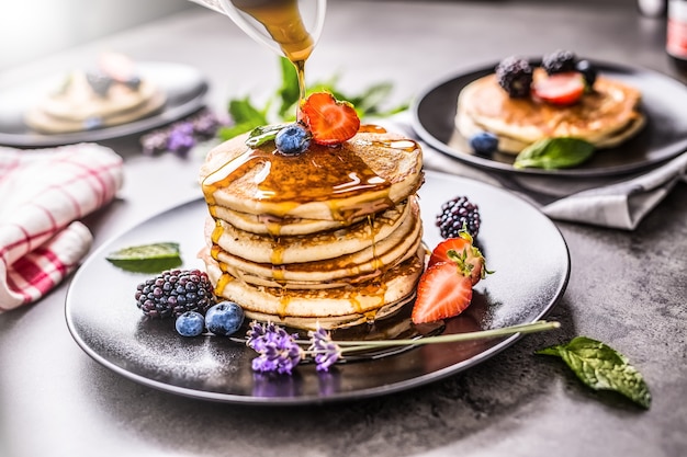 Pancakes with strawberries blackberries blueberries levander mint leaves and maple syrup.