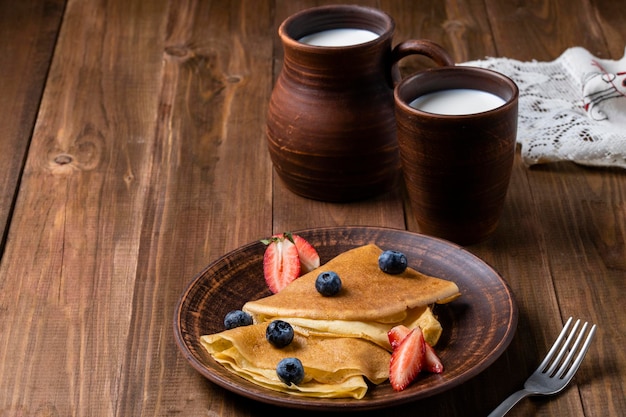 Pancakes with strawberries and blueberries jug with milk ceramic dishes in the style of rustic