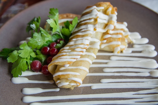 Pancakes with a stuffing on a ceramic plate with sour cream parsley and a cranberry on a ceramic plate.