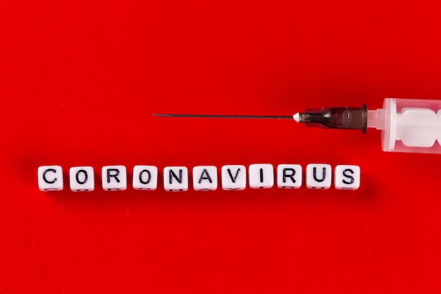 Pandemic and virus concept - Coronavirus text with syringe on red background. Novel coronavirus Covid-19.