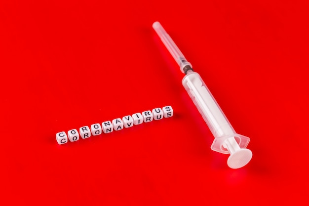 Pandemic and virus concept - Coronavirus text with syringe on red surface. Novel coronavirus Covid-19.