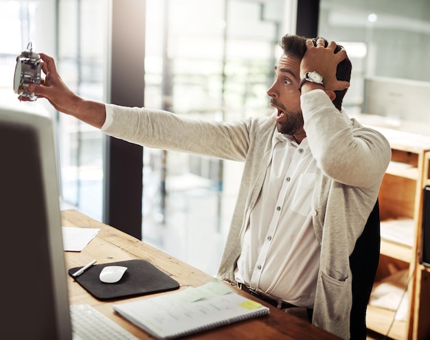 In a panic as his deadlines draw closer Shot of a handsome young businessman holding an alarm clock and looking stressed out while working late in an office