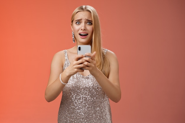 Panicking shocked woman concerned photos leaked internet look afraid anxious widen eyes cringing troubled hold smartphone shook speechless gasping terrified friends find out secret, red background.