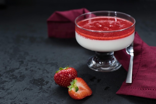 Panna cotta with strawberry sauce and strawberry berries in a bowl on the black background